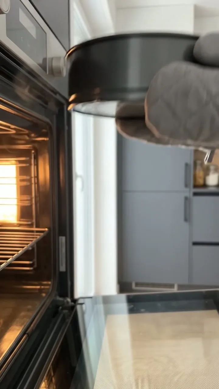 Oven mitts sliding the springform tin out of a glowing oven