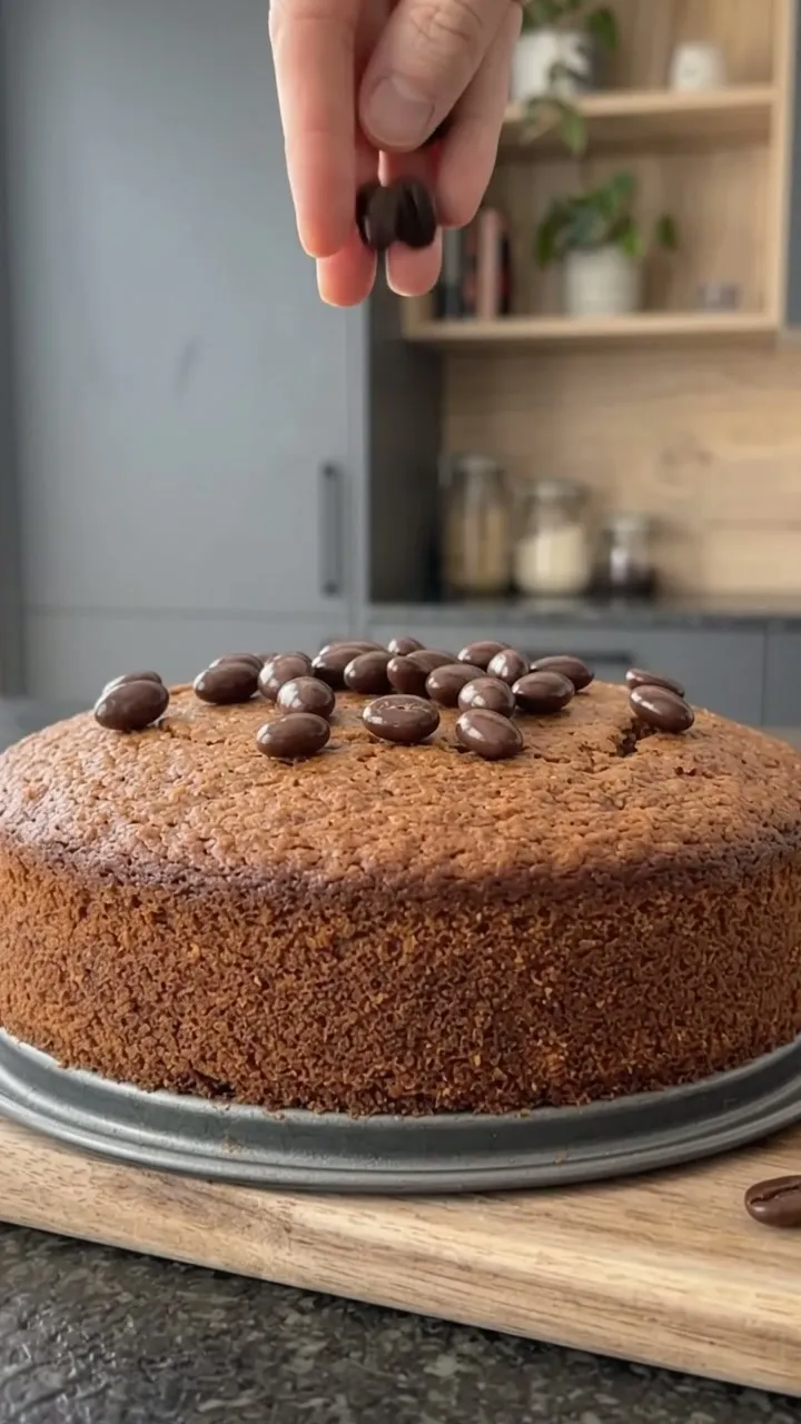 A hand scattering chocolate-covered espresso beans over the coffee cake