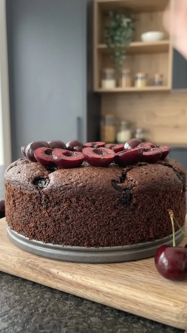 A hand placing halved fresh cherries on top of the chocolate cake